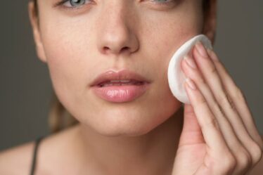 Young woman using a cotton pad for skincare, highlighting beauty routine.