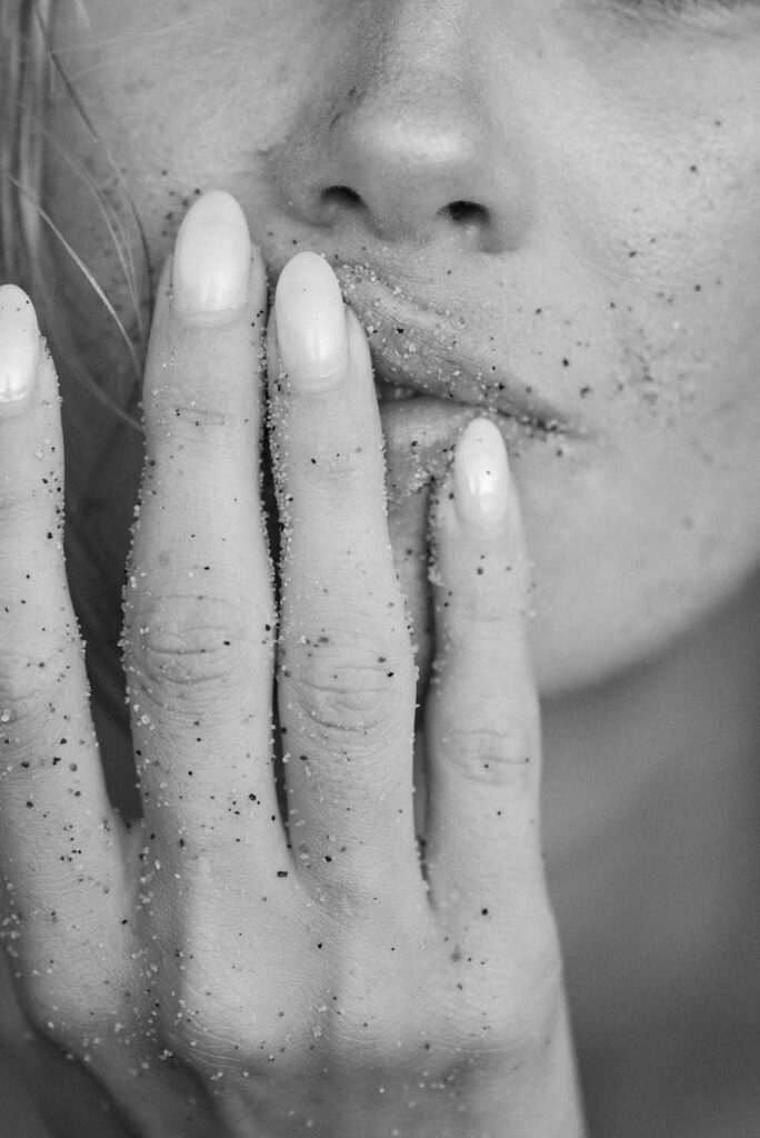 Close-up black and white image of a woman's sandy fingers touching her lips.