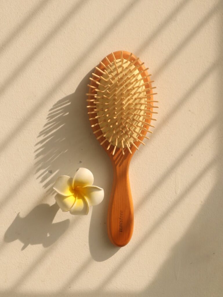 Wooden hair brush and white flower casting shadows on a light background, creating a minimalist composition.