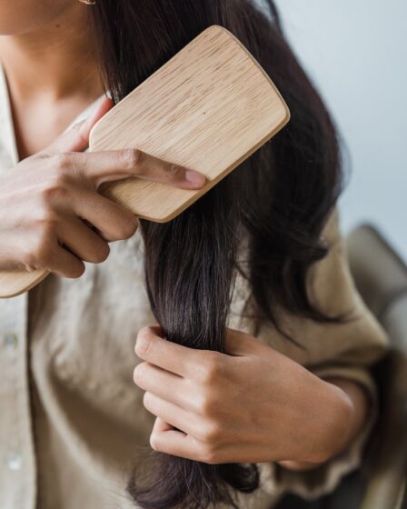 Close-up of a woman brushing her long dark hair with a wooden brush indoors.