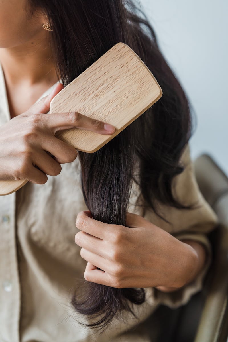 Close-up of a woman brushing her long dark hair with a wooden brush indoors.