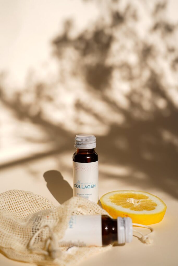 Luxurious glass cosmetic bottles with lemon slice and artistic shadows on a sunlit surface.