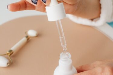 Close-up of hands using a dropper with a cosmetic bottle and jade roller, indoors.
