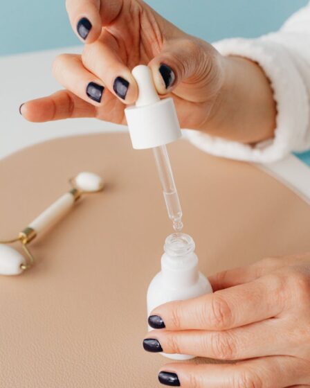 Close-up of hands using a dropper with a cosmetic bottle and jade roller, indoors.
