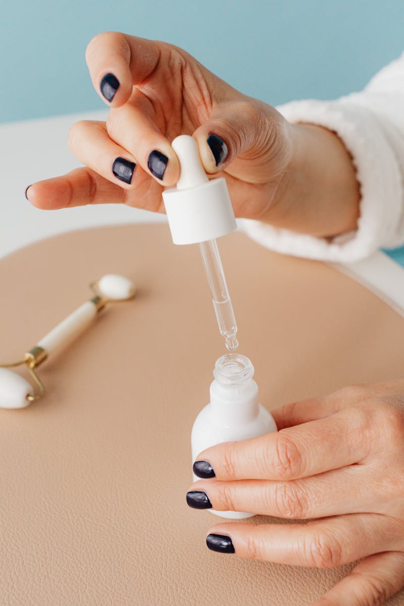 Close-up of hands using a dropper with a cosmetic bottle and jade roller, indoors.